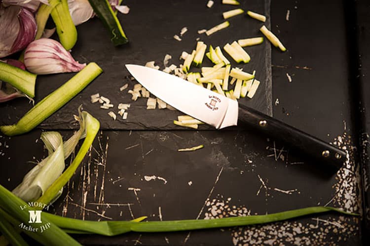 Couteau d'office posé sur une ardoise avec des légumes découpés