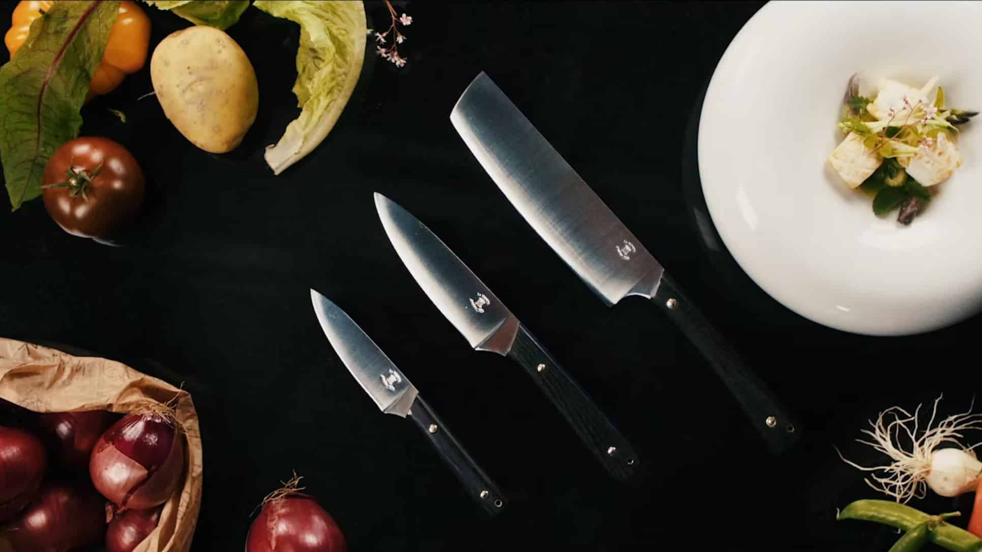 Couteaux de cuisine de l'atelier JHP, au milieu de fruits et légumes ainsi que d'une assiette gastronomique